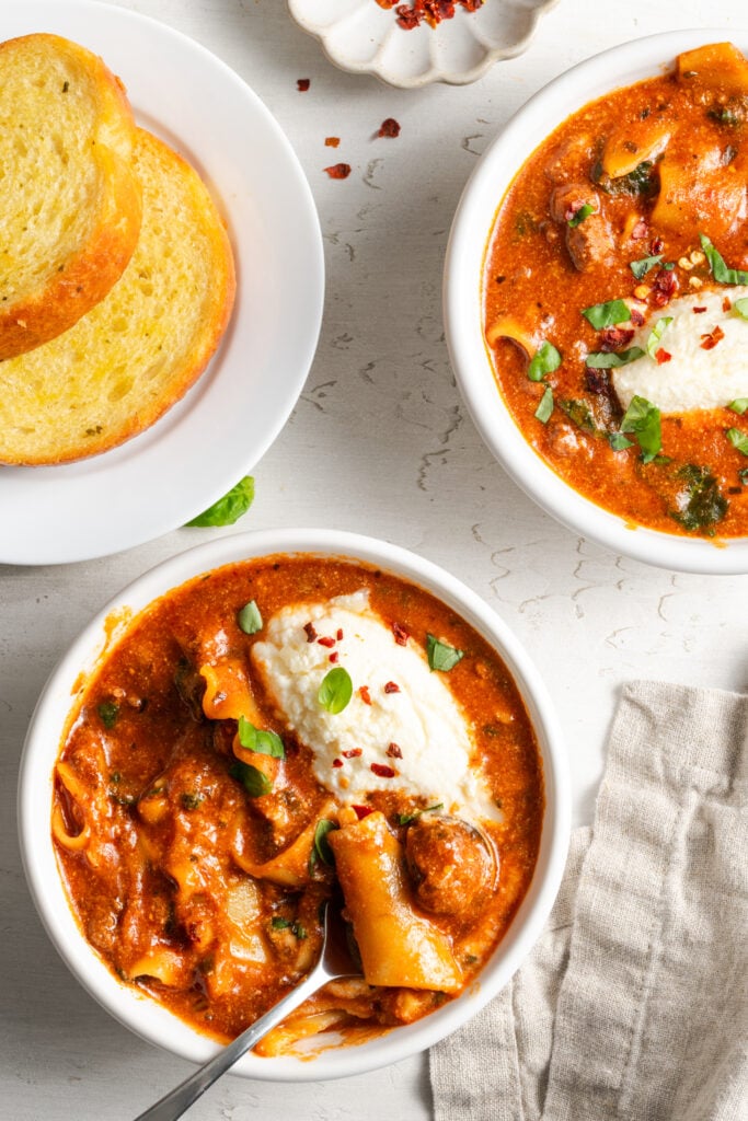 white table with two bowls of crock pot lasagna soup and a plate of toasted, buttered bread.