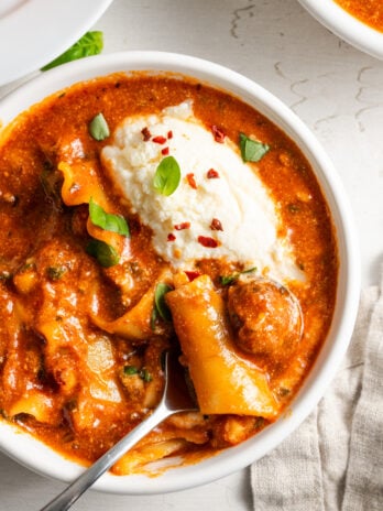 closeup overhead shot of a serving of easy slow cooker lasagna soup garnished with a dollop of ricotta and fresh herbs.