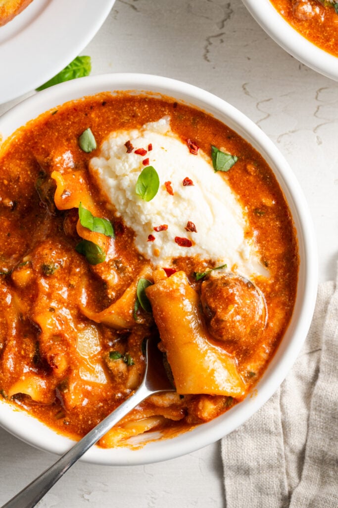 closeup overhead shot of a serving of easy slow cooker lasagna soup garnished with a dollop of ricotta and fresh herbs.