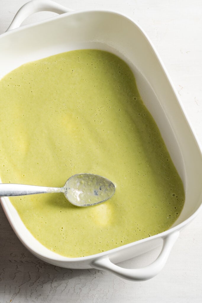 green enchilada sauce spread out in a thin layer on the bottom of a baking dish.