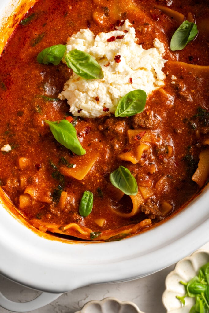 overhead closeup shot of lasagna soup in the slow cooker with a dollop of the cheese mixture and fresh basil leaves.