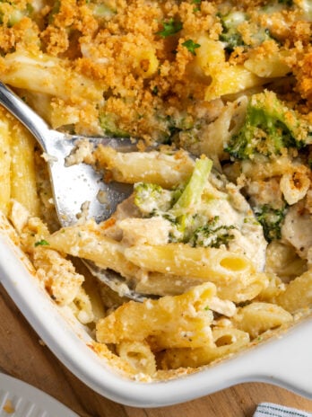 closeup shot of the corner of the baking dish with a silver serving spoon dishing out some of the creamy broccoli chicken alfredo, showing the contrast with the crunchy breadcrumbs on top.
