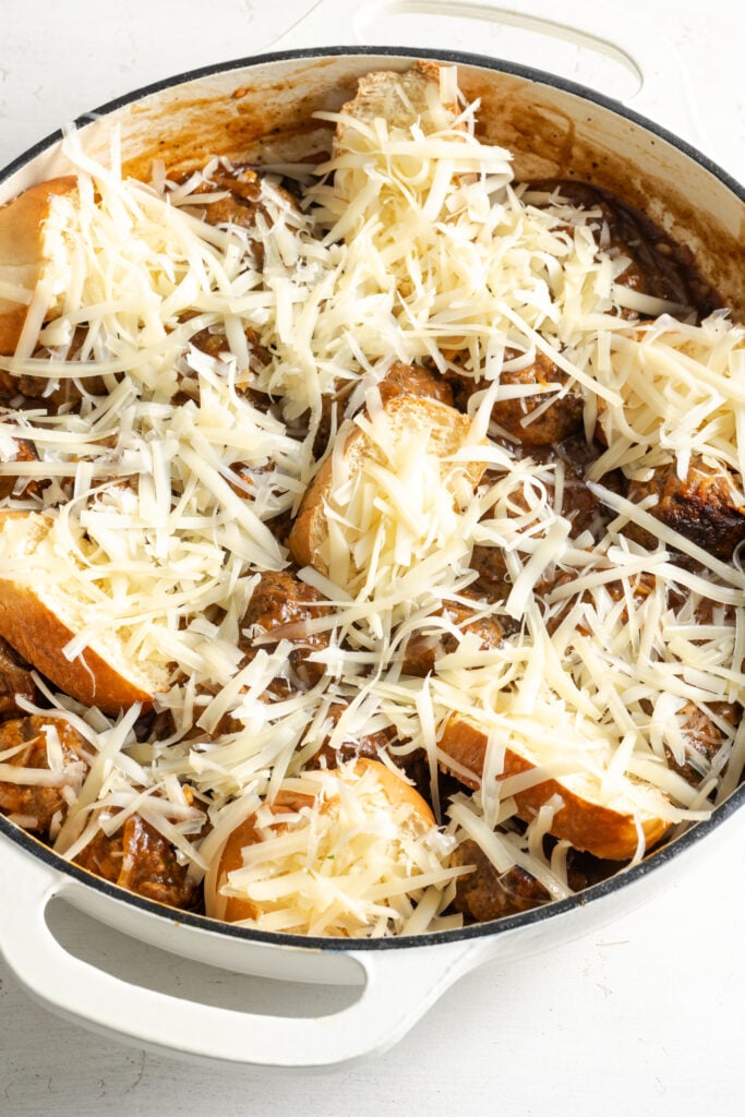 french bread slices and shredded cheese added to the white baking dish on top of the french onion meatballs and gravy before broiling.