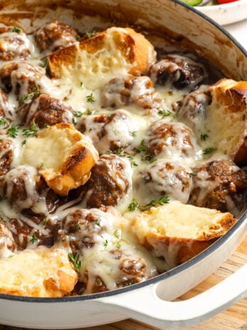 closeup shot of french onion meatballs in the white pan after adding toast points and melted cheese and broiling.