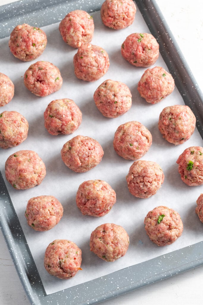 raw french onion meatballs on a parchment lined baking sheet before baking.