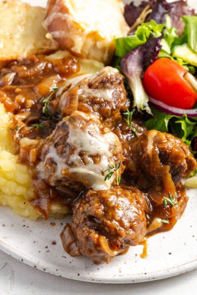 closeup shot of ground beef french onion meatballs on top of mashed potatoes with a side salad.