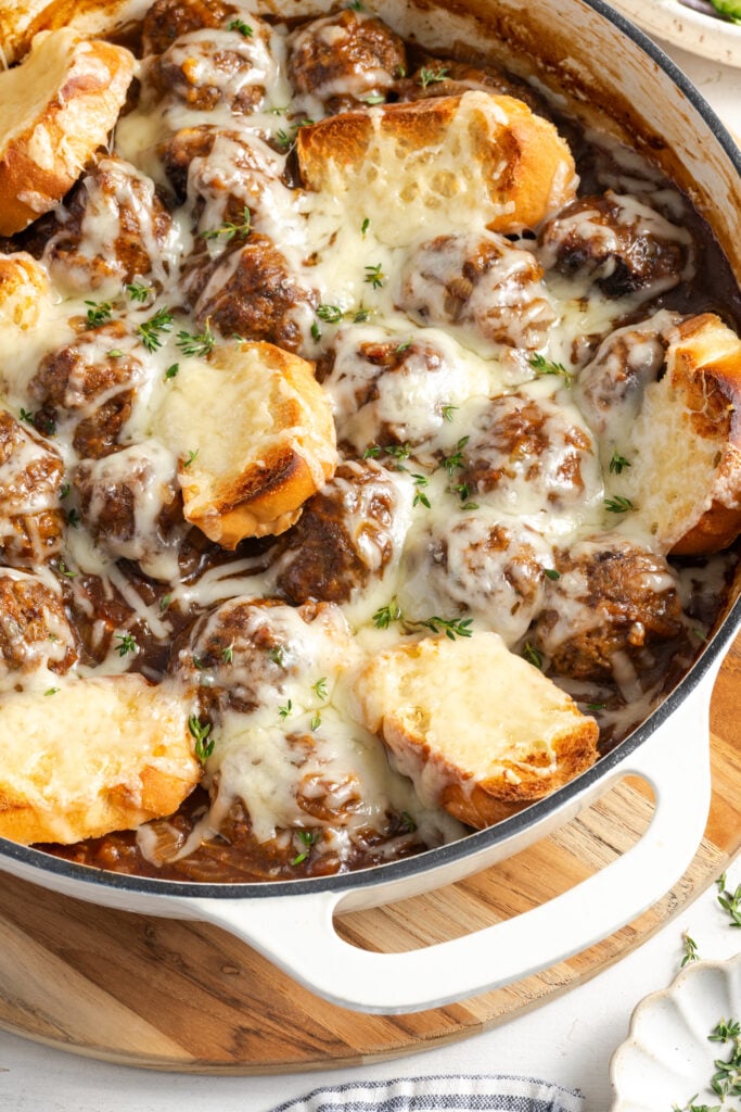 closeup shot of the white baking dish filled with french onion meatballs topped with gruyere cheese and toast.