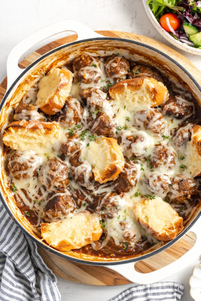 overhead shot of the baking dish with the french onion meatballs after adding the sliced french bread and cheese and broiling.