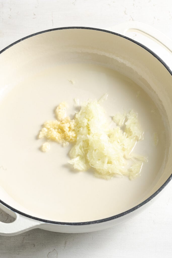 minced garlic and onion added to a shallow white dutch oven with oil.