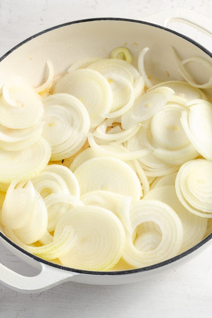 raw slices of onions added to a shallow white dutch oven to saute.