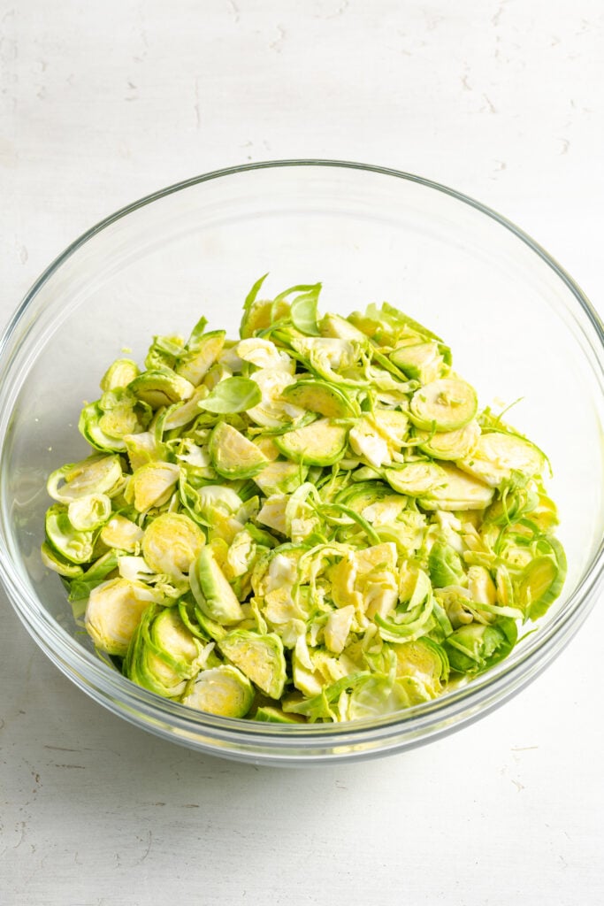 plain raw shaved brussels sprouts in a clear mixing bowl.