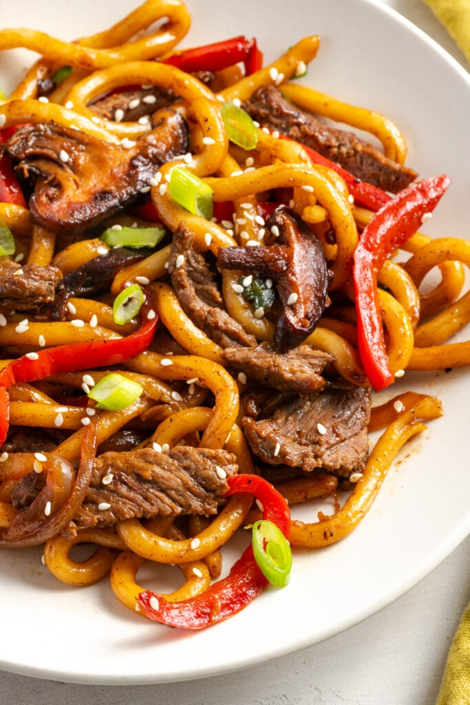 beef noodle stir fry on a white pasta plate.