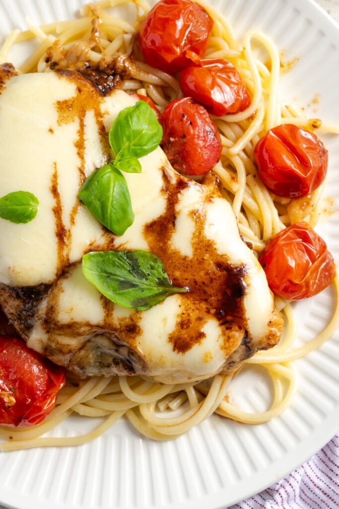 closeup overhead shot of skillet caprese chicken with pasta on a white dinner plate.