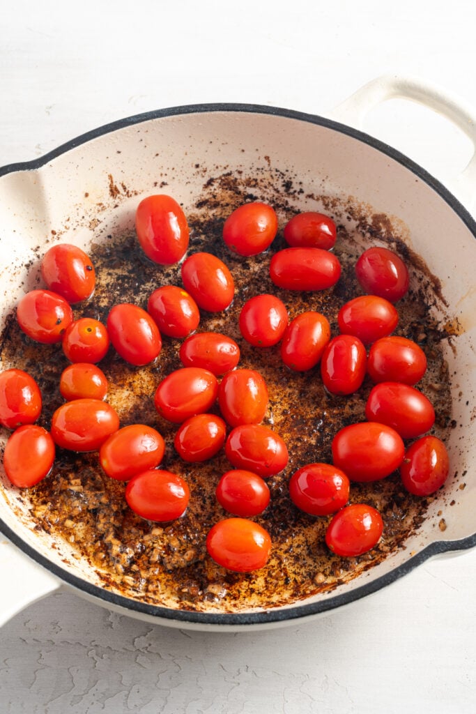 cherry tomatoes added to the skillet with the chicken fond.