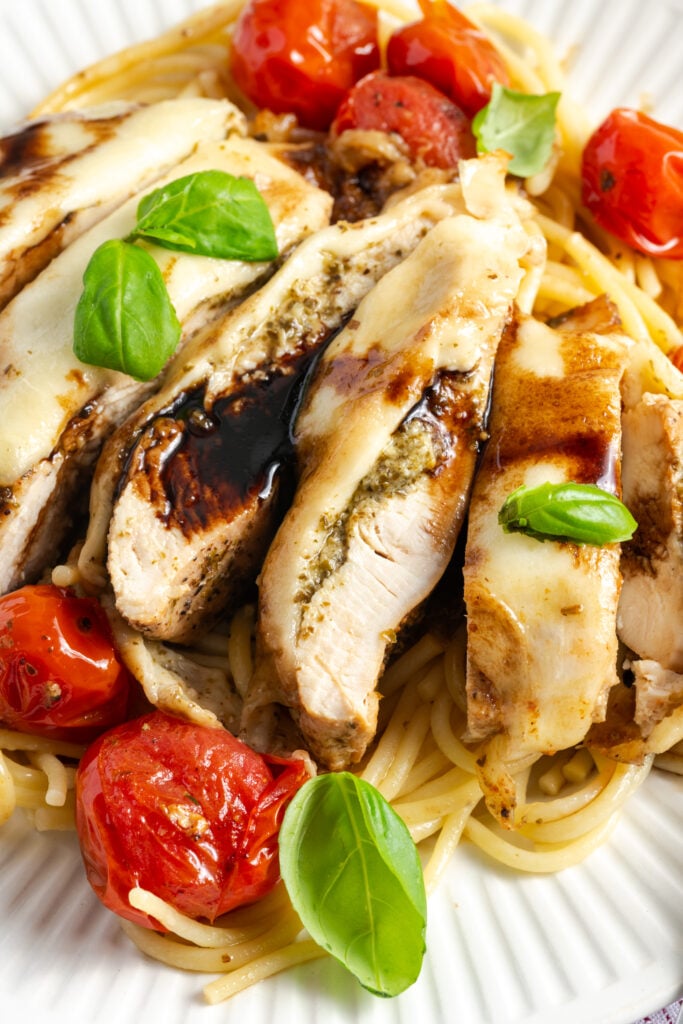 sliced chicken caprese on a bed of pasta showing the layer of pesto underneath the melted cheese.