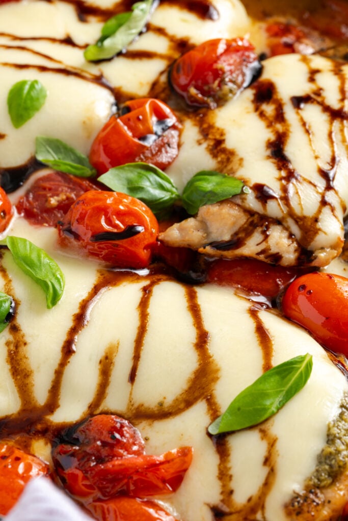 closeup shot of caprese chicken in a skillet showing the melty cheese, roasted cherry tomatoes, fresh basil, and balsamic drizzle.