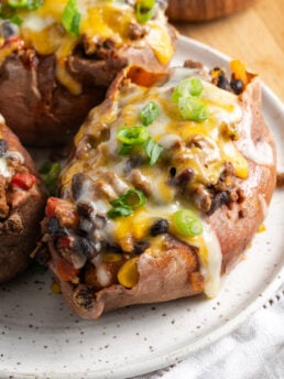 closeup shot of an assembled ground beef stuffed sweet potato topped with melty cheese and scallions.