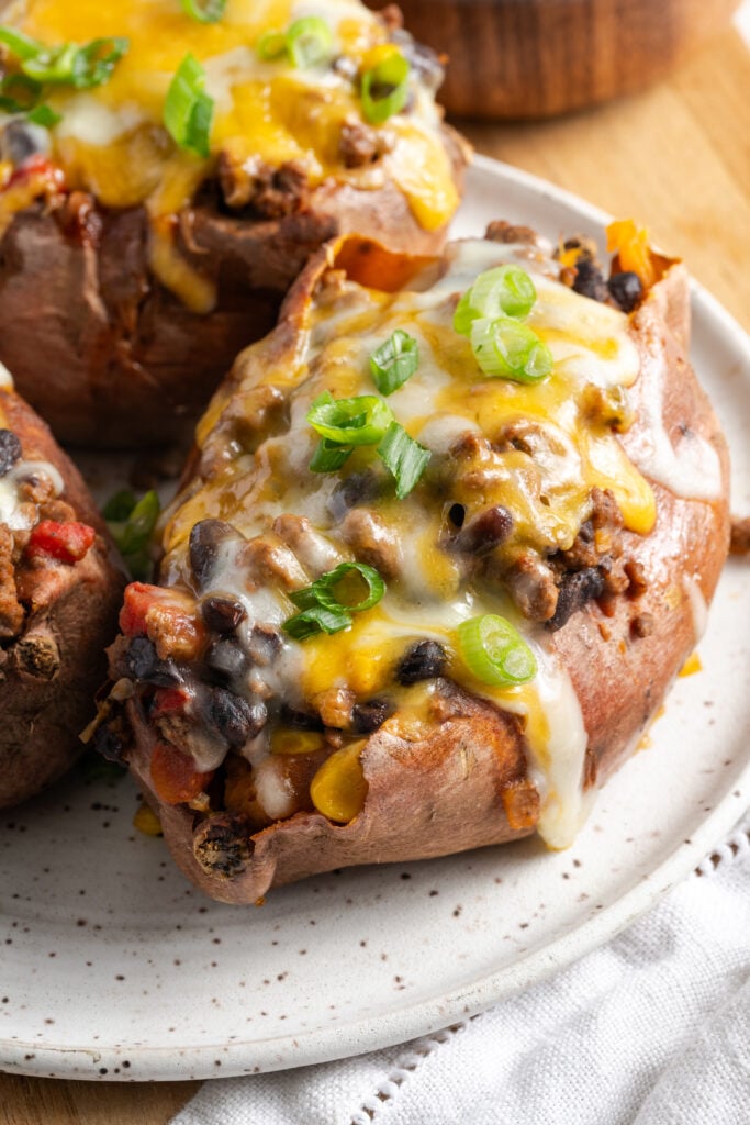 closeup shot of an assembled ground beef stuffed sweet potato topped with melty cheese and scallions.