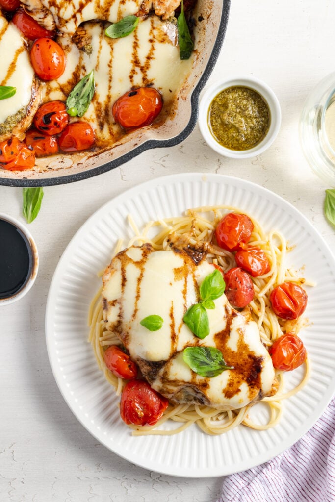 overhead shot of a plate of caprese chicken served on a bed of pasta with the remaining servings still in the skillet.