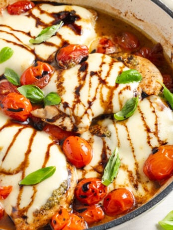 closeup shot of skillet caprese chicken in the skillet after drizzling with balsamic reduction and sprinkling on fresh basil.