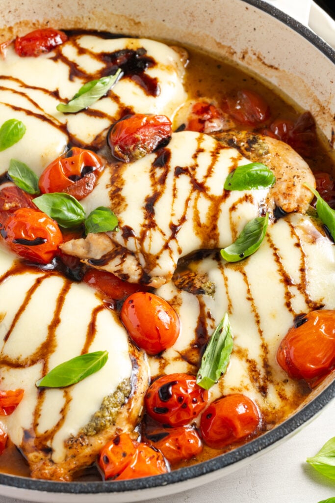 closeup shot of skillet caprese chicken in the skillet after drizzling with balsamic reduction and sprinkling on fresh basil.