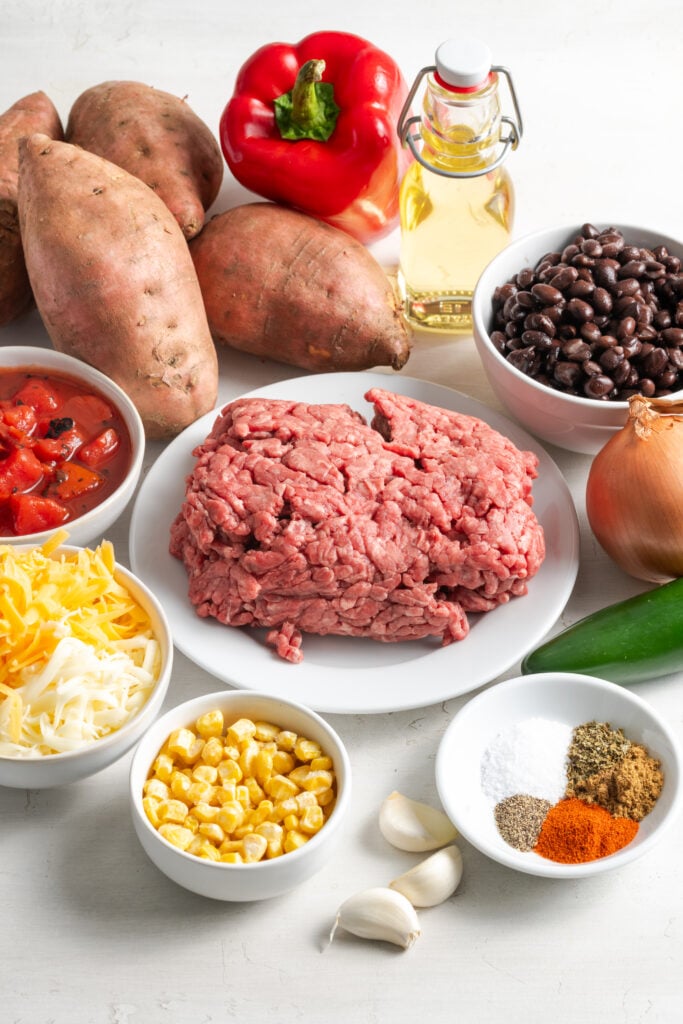 ingredients needed to make ground beef and black bean taco stuffed sweet potatoes measured out on a white table.