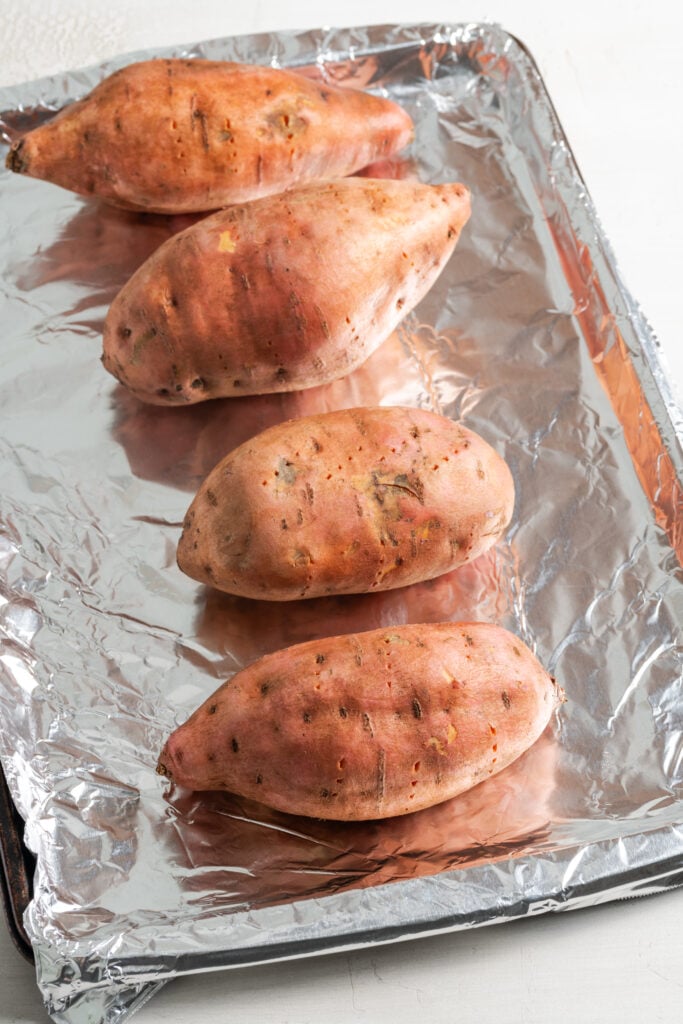 raw sweet potatoes on a foil lined baking sheet.