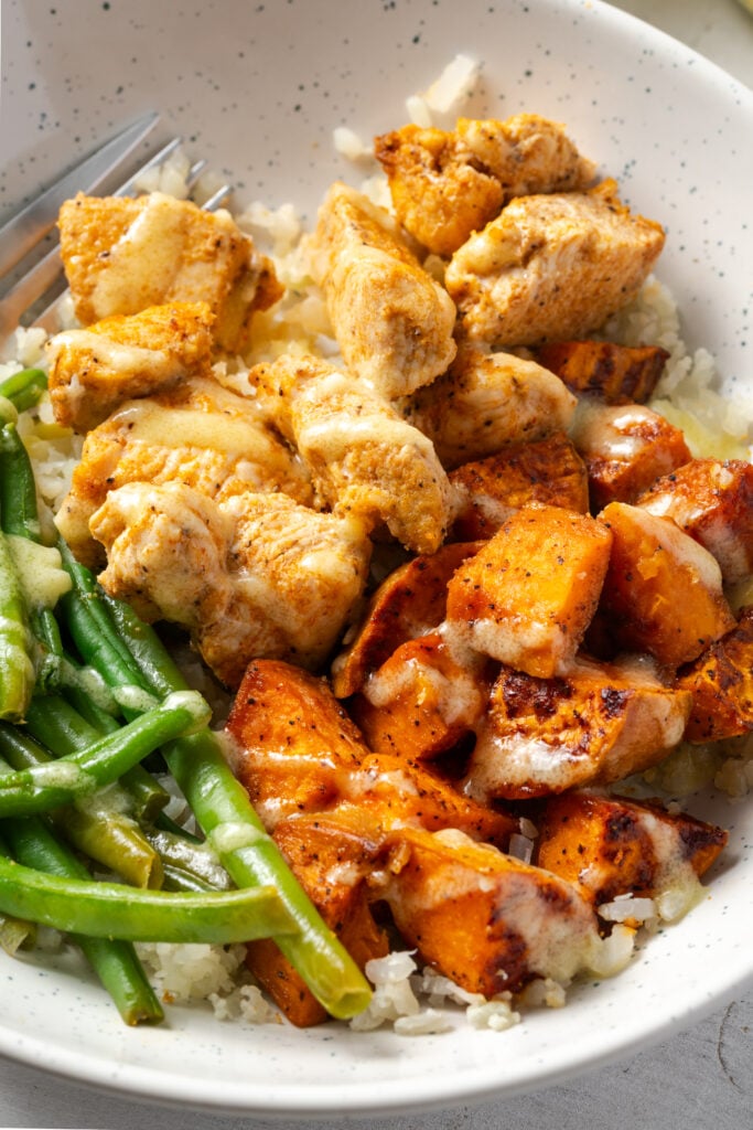 closeup shot of chicken and sweet potato bowl with garlic mojo sauce and green beans.