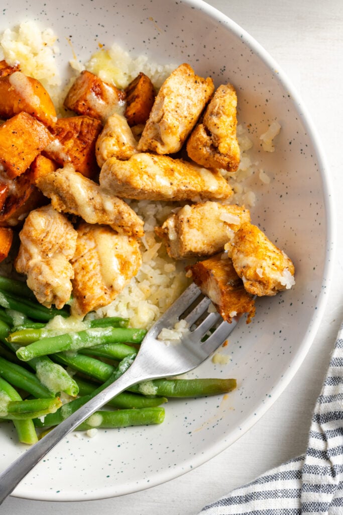 closeup overhead shot of a silver fork taking a bite of chicken and roasted sweet potato from the bowl