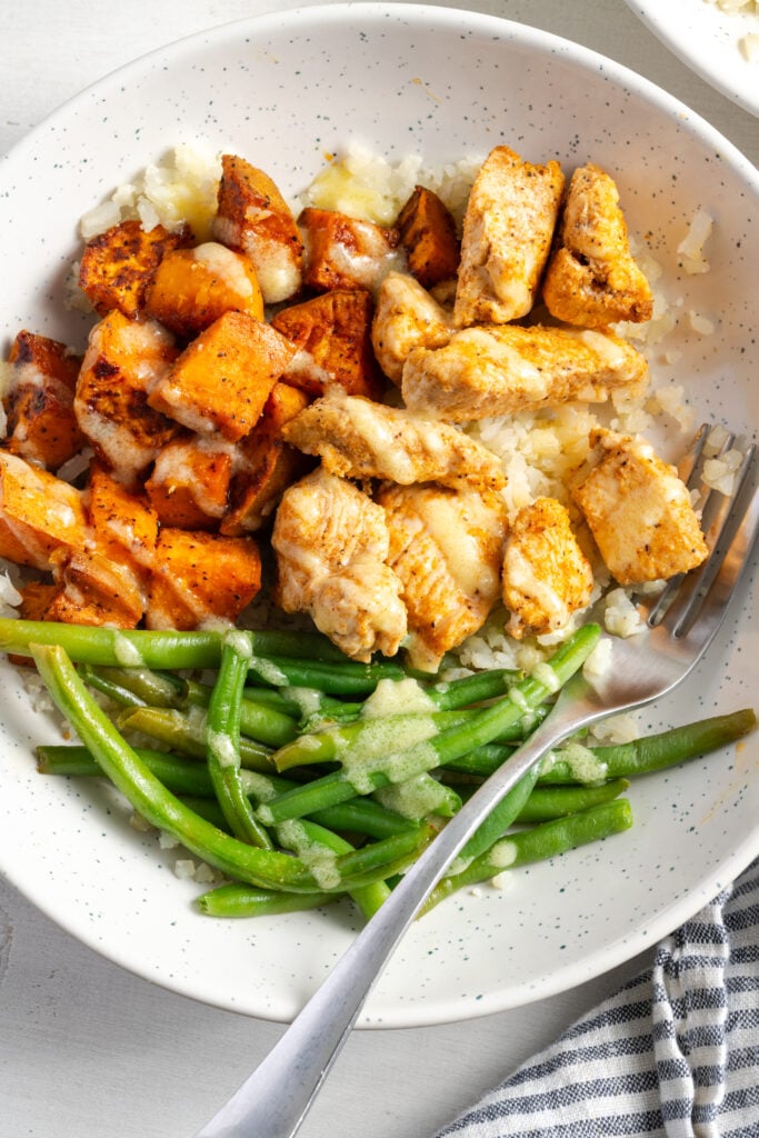 flat lay shot of a chicken sweet potato bowl with green beans, cauliflower rice and mojo sauce.