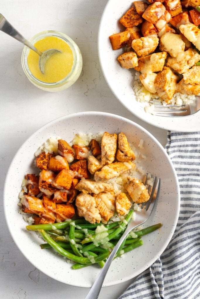 flat lay shot of two mojo chicken sweet potato bowls drizzled with creamy garlic mojo sauce.