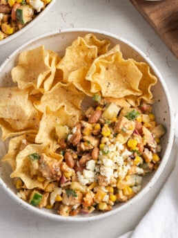 overhead shot of a bowl half filled with high protein salad and the other half filled with tostitos scoops chips for scooping.