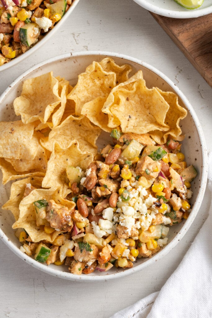 overhead shot of a bowl half filled with high protein salad and the other half filled with tostitos scoops chips for scooping.