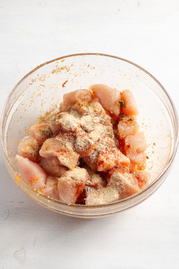 raw chicken chunks in a mixing bowl with seasonings.
