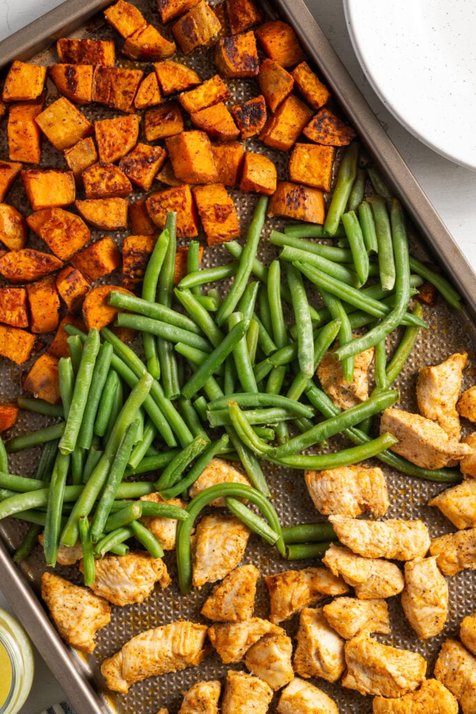 overhead shot of roasted sweet potatoes, green beans, and chicken on a sheet pan.