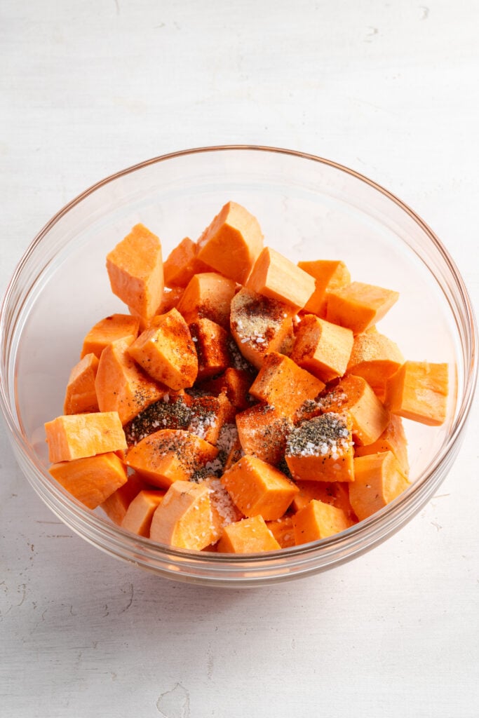 sweet potato cubes in a mixing bowl with oil and seasonings.