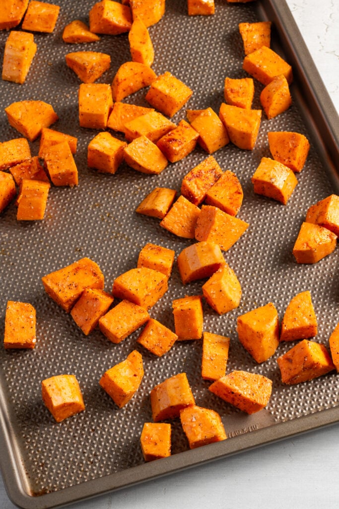 seasoned sweet potatoes on a sheet pan before roasting.