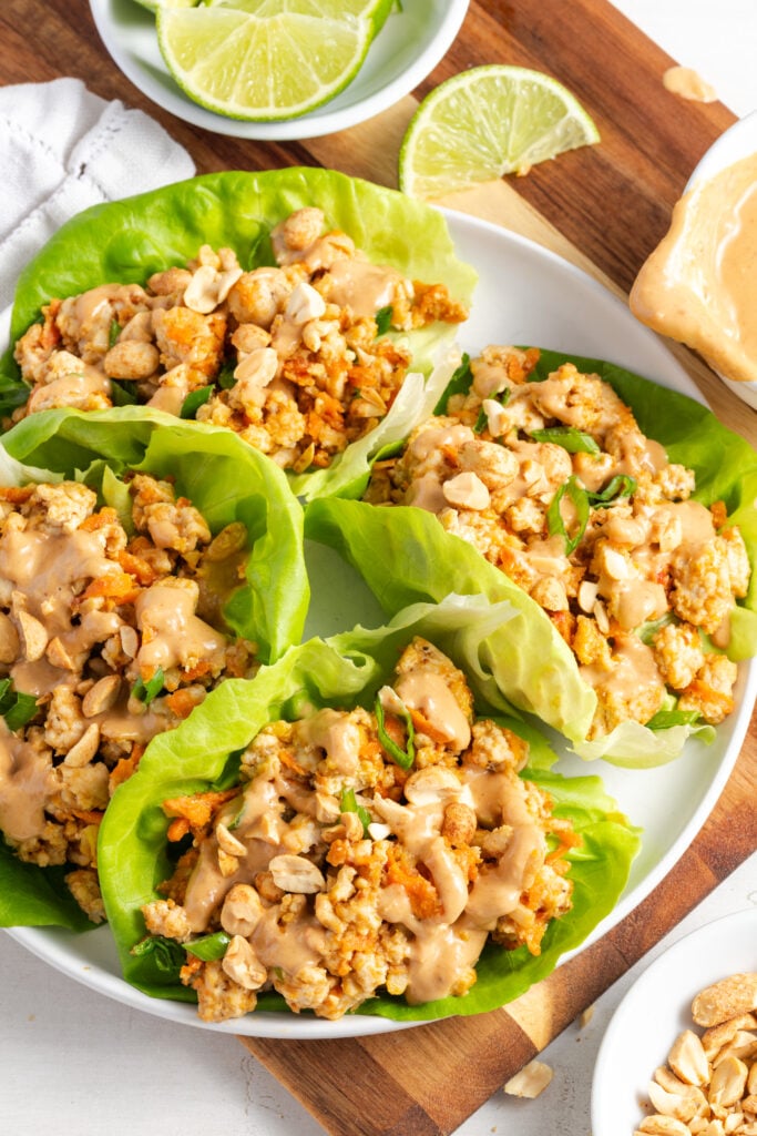 4 asian ground turkey lettuce wraps on a white serving platter on a wooden cutting board.