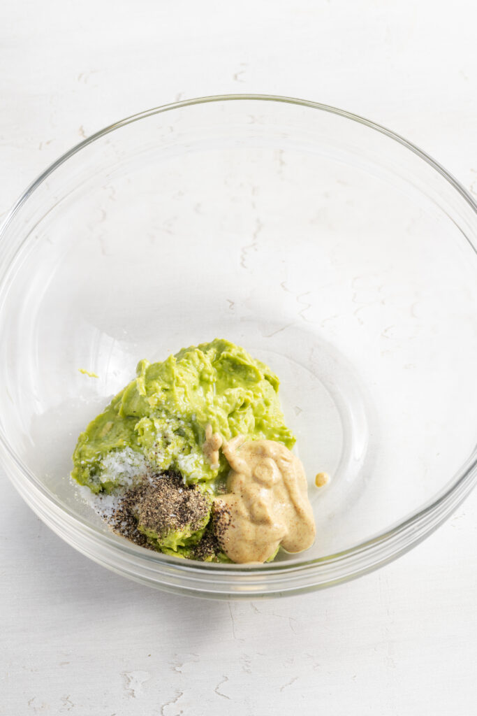 mashed avocado, mustard, and seasonings added to a mixing bowl for making the dressing.
