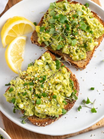 flat lay shot of avocado and egg salad on toast with lemon wedges.