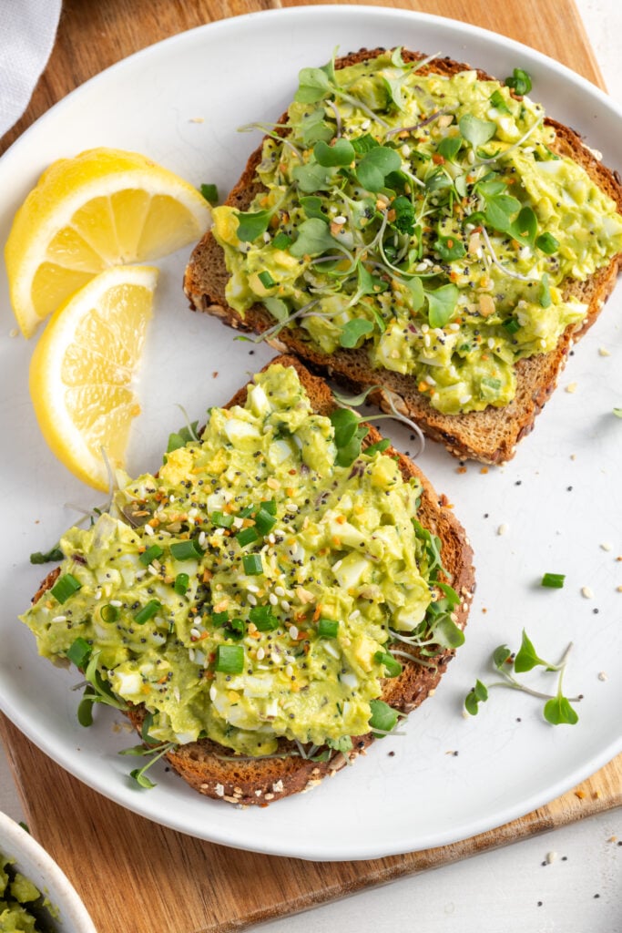 flat lay shot of avocado and egg salad on toast with lemon wedges.