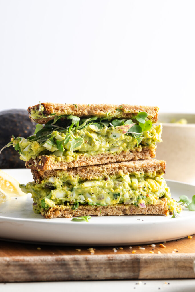 closeup side on shot of a halved avocado egg salad sandwich with microgreens.