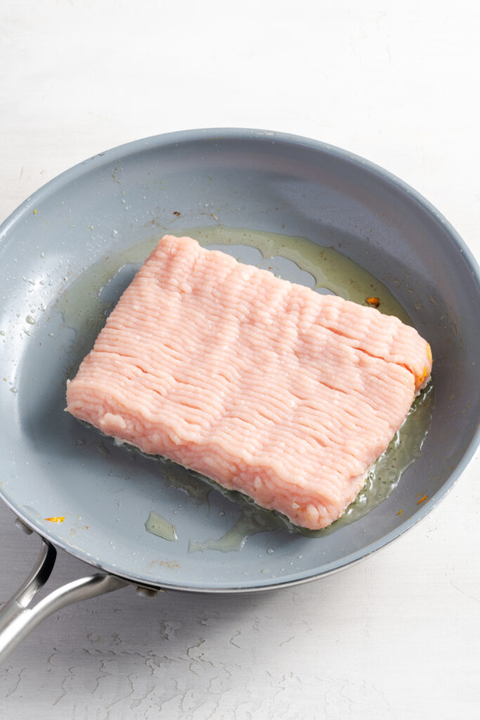 raw ground turkey added to a pan with oil.