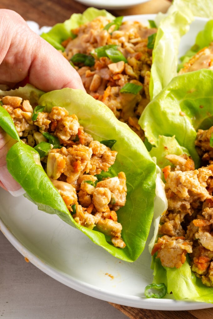 hand grabbing a ground turkey lettuce wrap from the white serving platter.