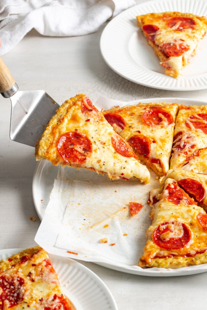pie server grabbing a slice of chicken crust pepperoni pizza from the plate.