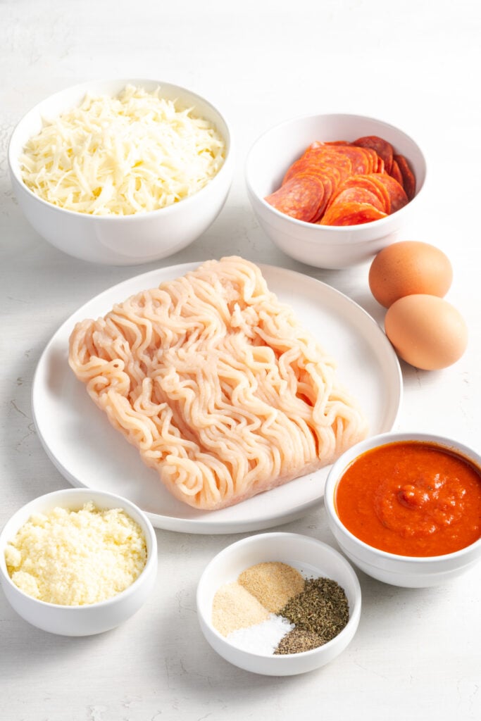 ingredients needed to make chicken crust pizza recipe measured out in white bowls on a white table.