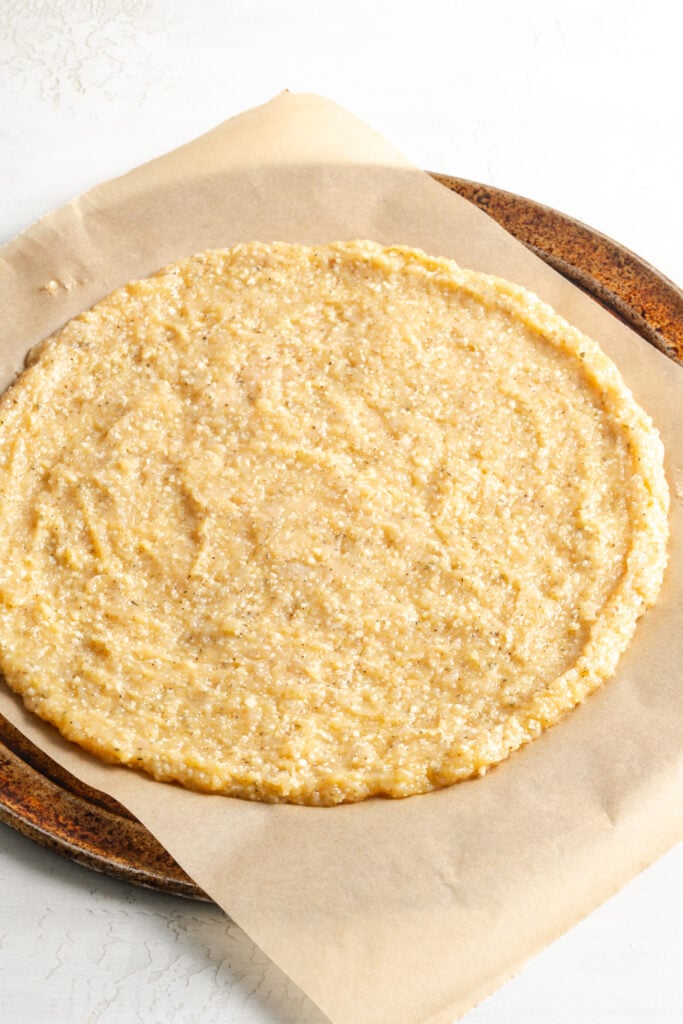 chicken pizza crust shaped out on a piece of parchment paper before baking.