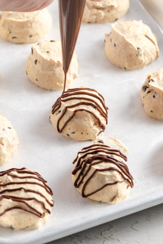 action shot of a piping bag being used to drizzle frozen peanut butter yogurt bites with chocolate.