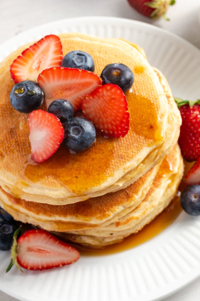 closeup shot of fluffy cottage cheese pancakes topped with sliced strawberries and fresh blueberries.
