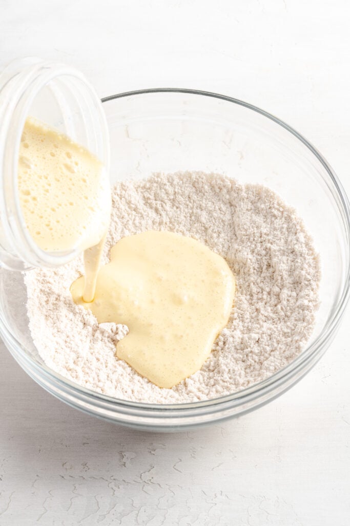blended wet ingredients being poured into a bowl with the dry ingredients to make easy cottage cheese pancakes.